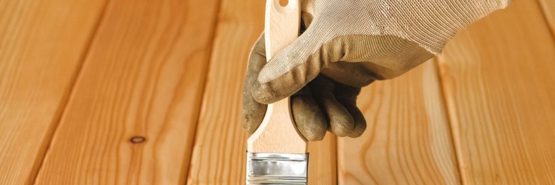 Man hand in a glove holding a brush on natural wooden boards background.